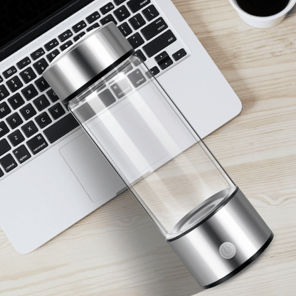 Clear and silver water bottle on a desk with a laptop and coffee cup.