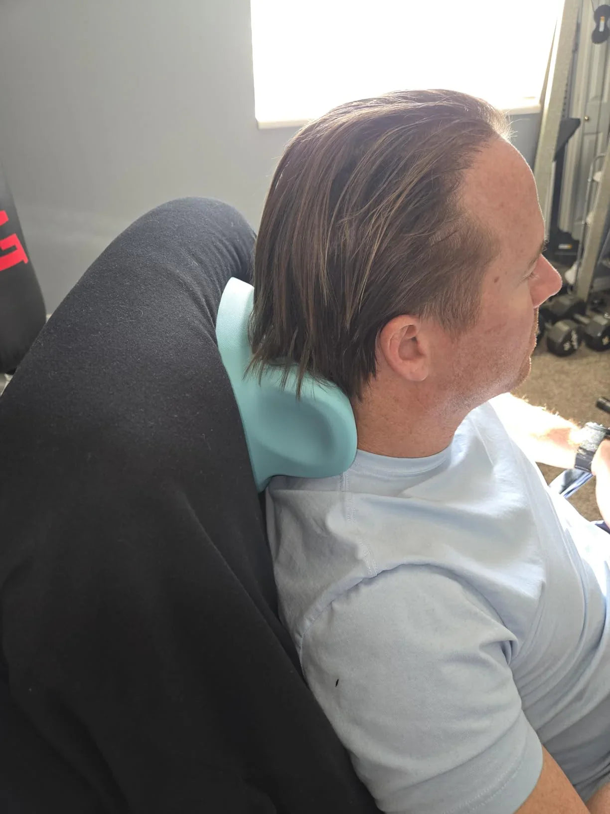 Person using a neck massager on a couch in a living room.