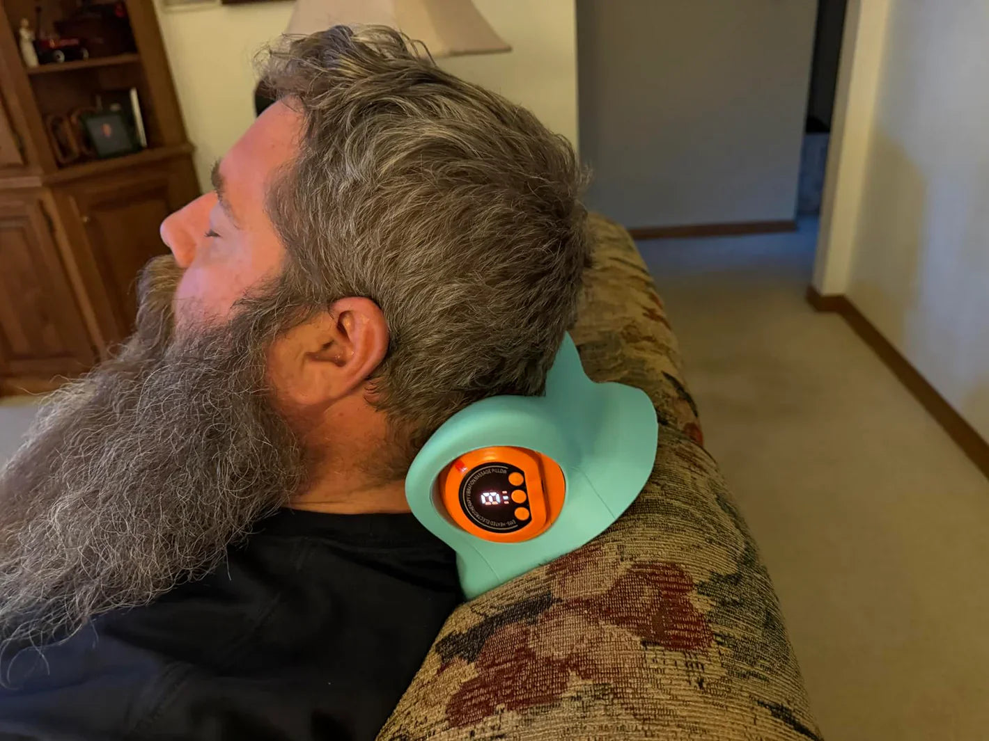 Person using a neck massager on a couch in a living room.